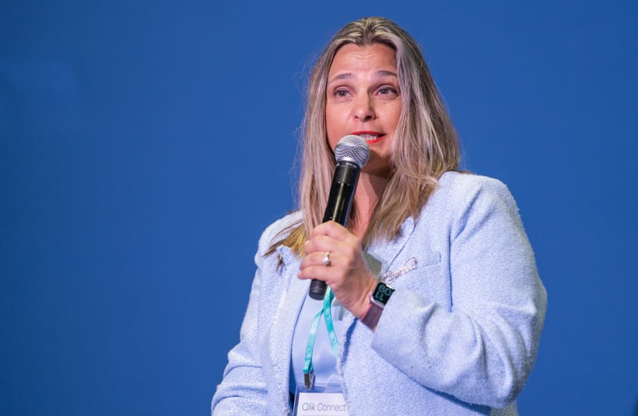 A speaker at Qlik Connect addresses the audience with a microphone in hand, sharing insights on stage against a blue backdrop.
