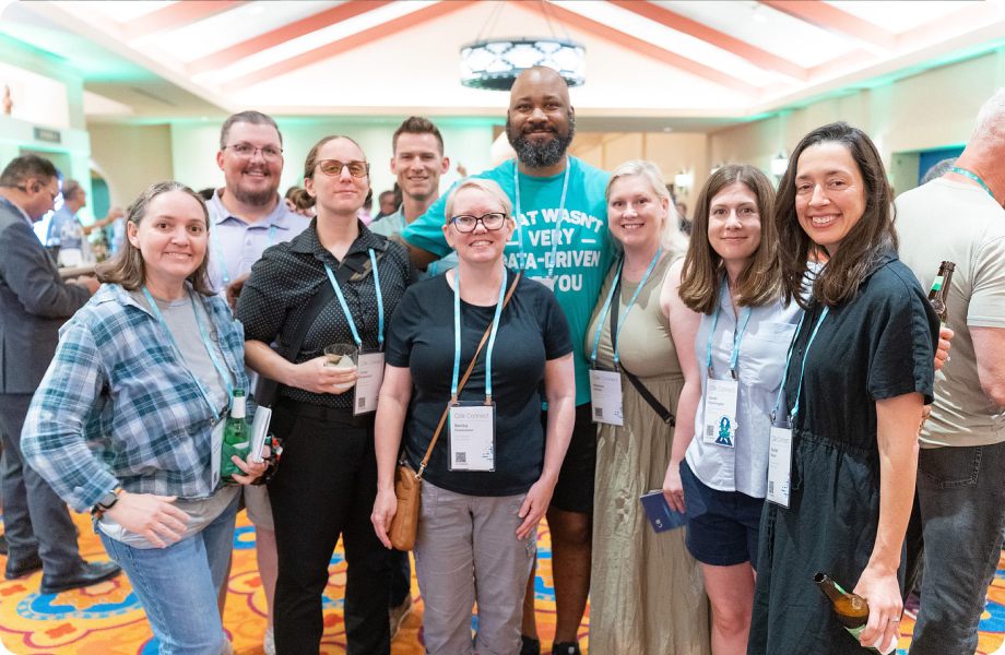 A group of nine smiling attendees wearing lanyards posing for a photo at a conference.
