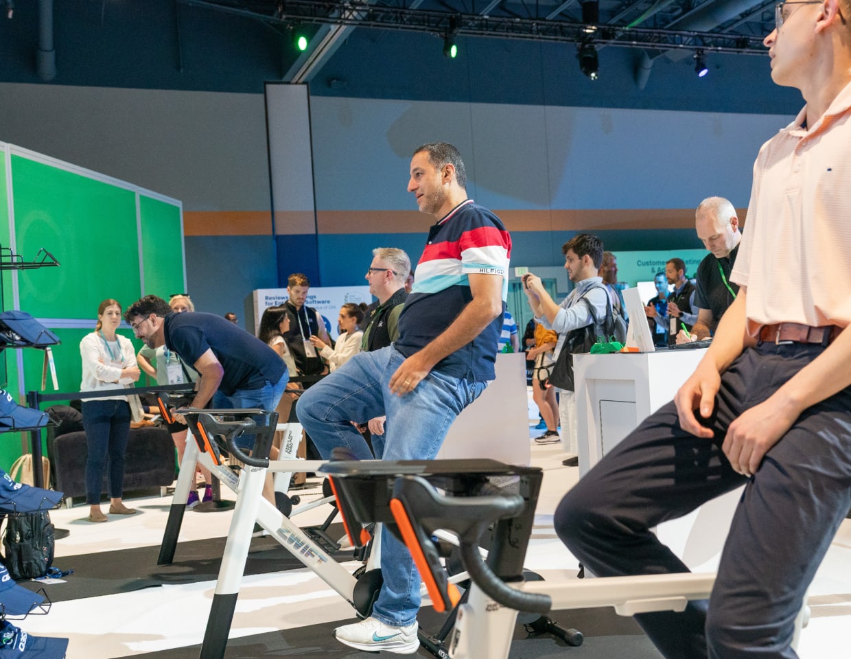 Attendees participate in an interactive cycling activity at a Qlik event, engaging with data-driven fitness displays and networking around various demo stations in a lively exhibition environment.