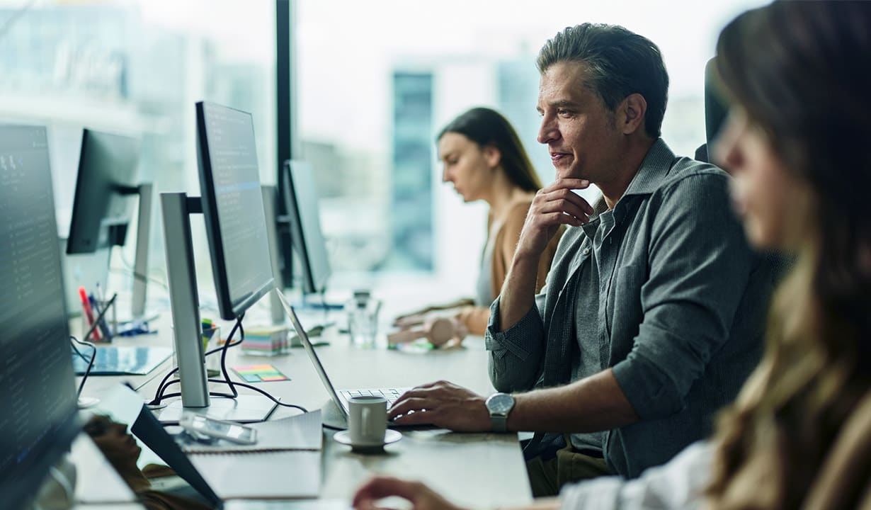 A diverse group of professionals focused on their computers, working together in a bright, open office space.