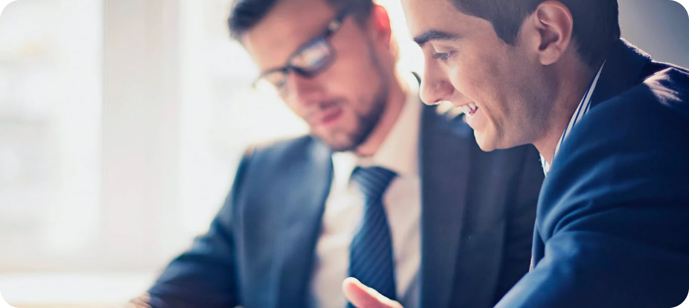 Image of two men in business suits sitting at a table, looking at documents in an office.