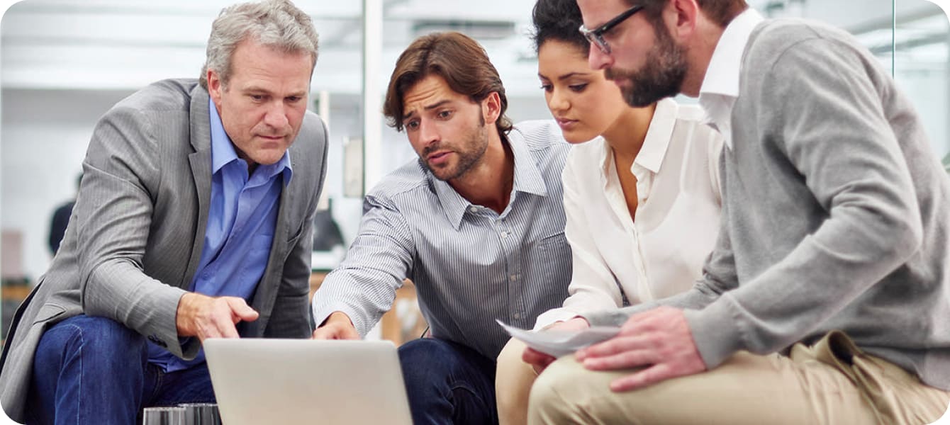 Image of several individuals engaged in teamwork at a computer, sharing insights and working on a project together.