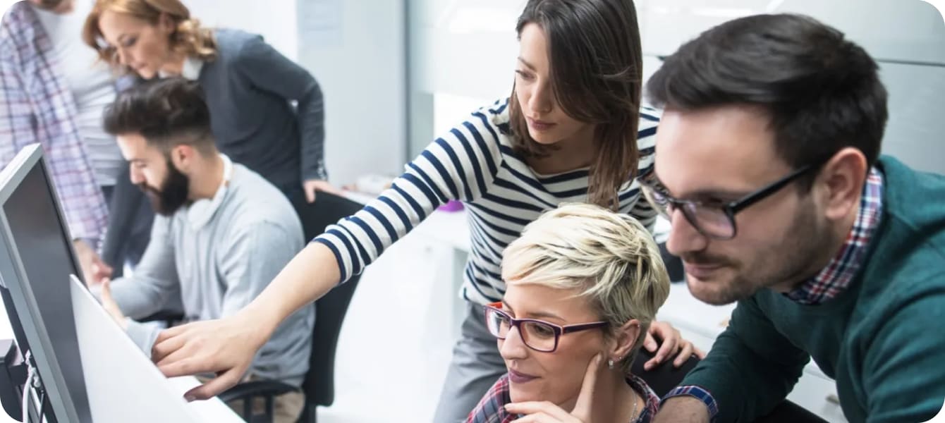 An image of several individuals engaged in teamwork at a computer, sharing insights and working on a project together.