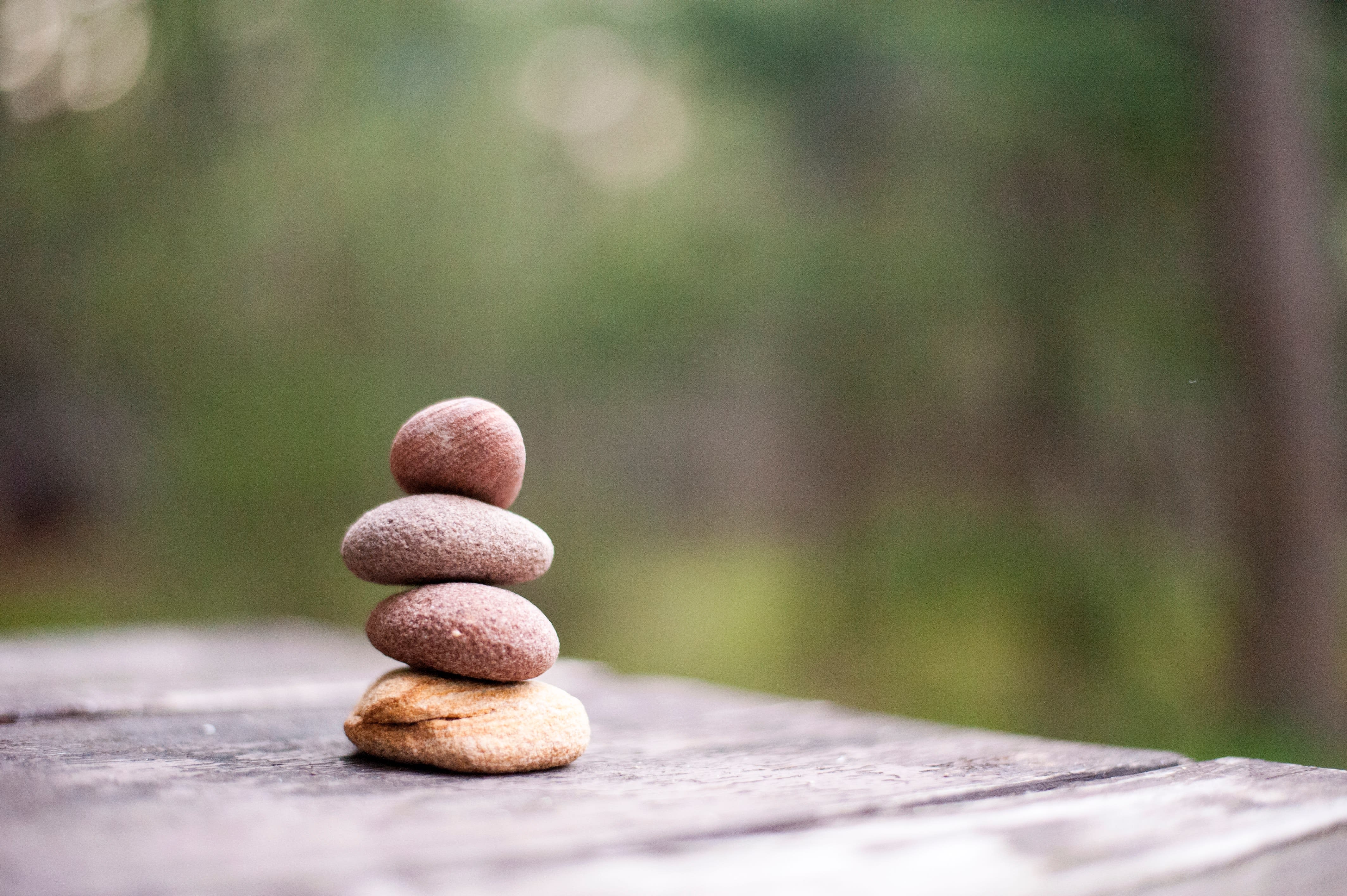 A stack of four smooth stones balancing on a wooden surface with a blurred green background.