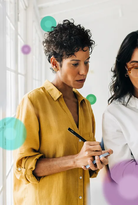 Two women in an office engaged in discussion while one takes notes.