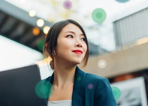 A woman in a business suit confidently holds a laptop looking into the distance with a smile