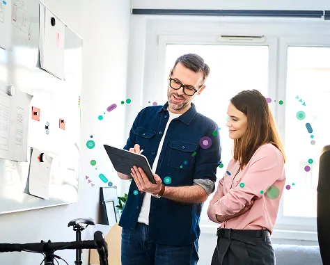 A man and woman stand by a whiteboard displaying various icons, engaged in a discussion or presentation.