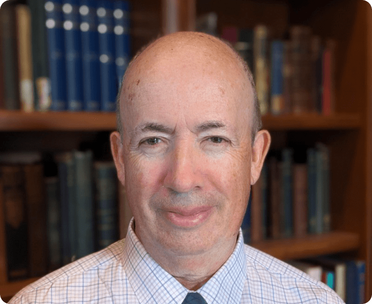 Portrait of Malcolm Chisholm, Ph.D., Senior Principal Advisor, in a suit and tie, smiling, with bookshelves in the background. 