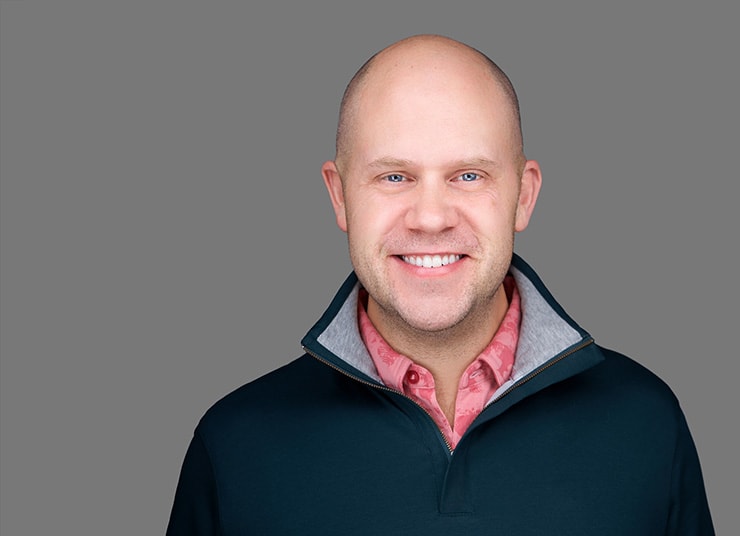 Sam Pierson, Chief Technology Officer at Qlik in a dark sweater and red shirt stands against a plain gray background, smiling into the camera.