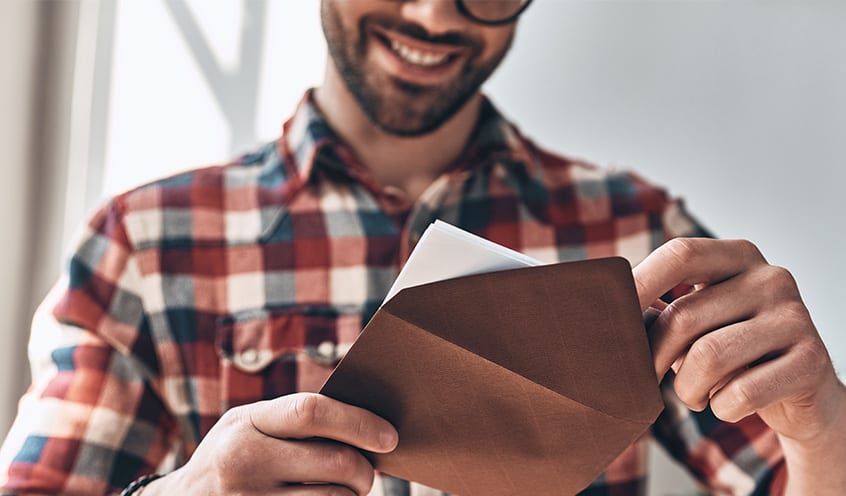 A man wearing a checkered shirt reads a letter from a brown envelope.