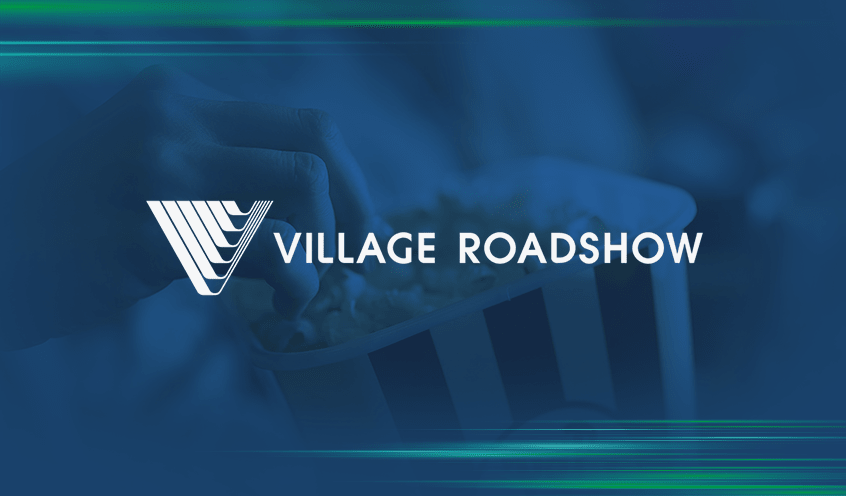 A hand reaching into a striped popcorn container with the Village Roadshow logo and text overlayed on a blue-tinted background.